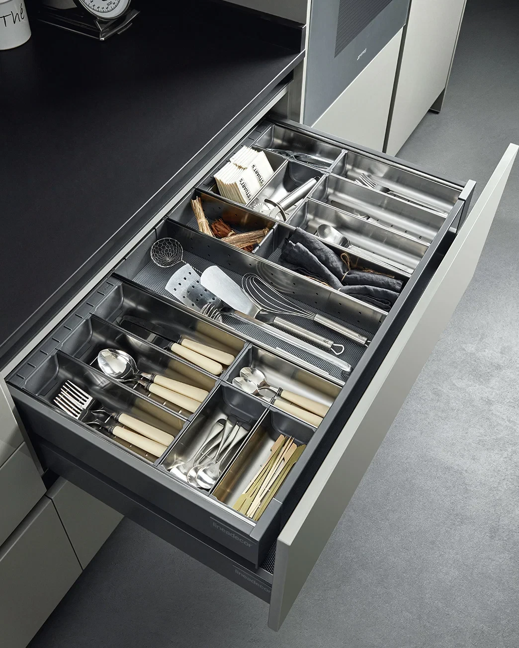 Kitchen utensils and cutlery organized in a stainless steel drawer.